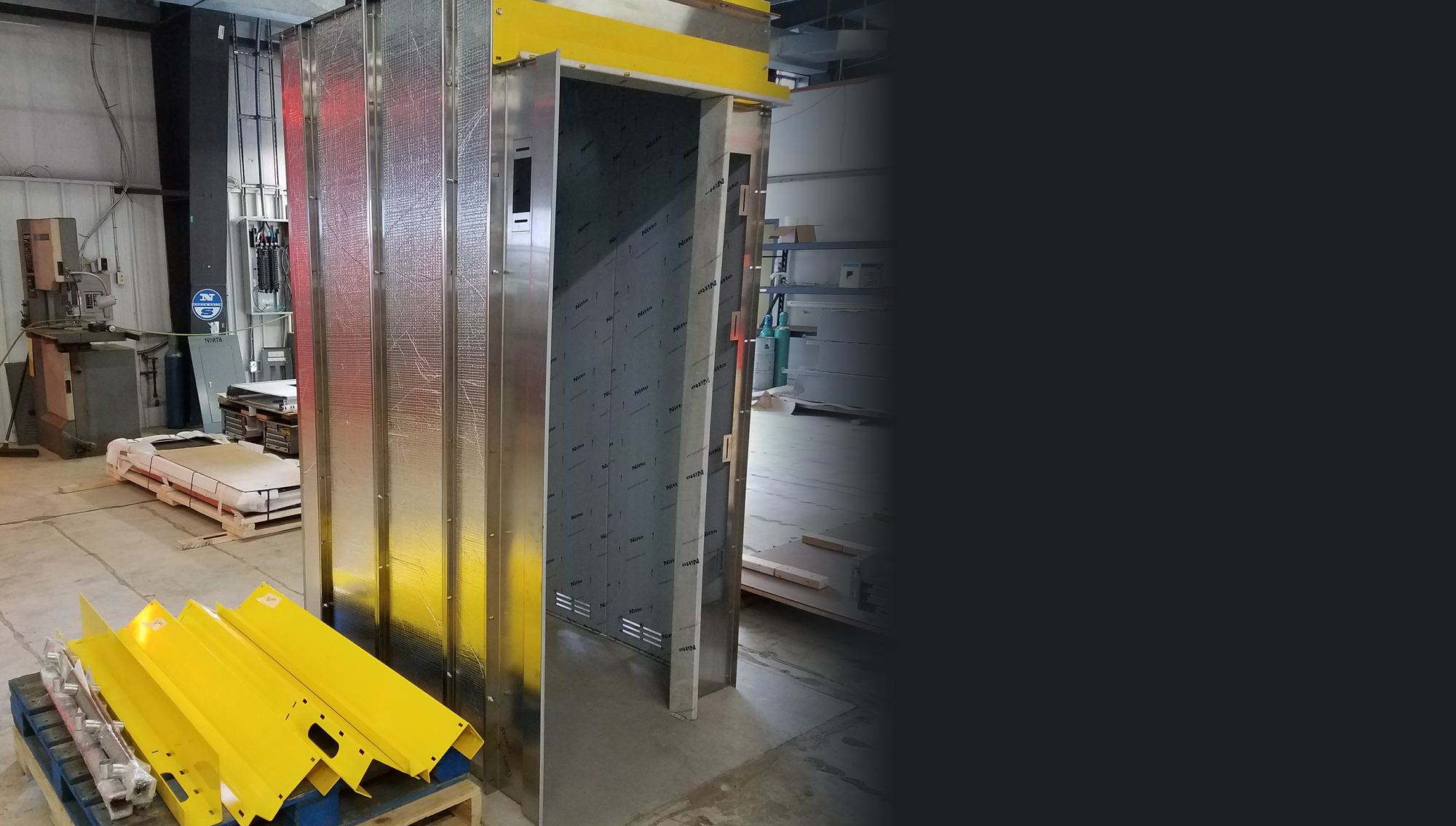 A CabCraft cab shell with stainless front walls hung and a pallet of powder-coated door operator supports